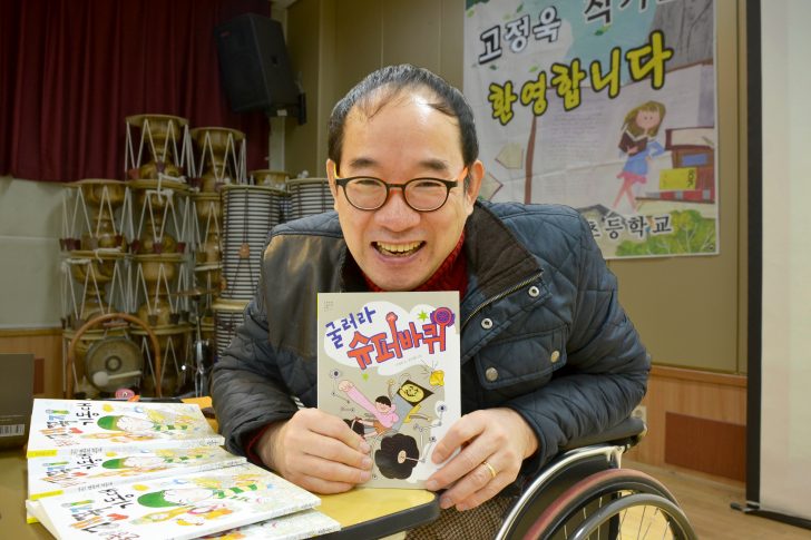 ▲ 고정욱 작가가 신간 <굴러라 슈퍼 바퀴>를 들고 환한 미소를 짓고 있다.