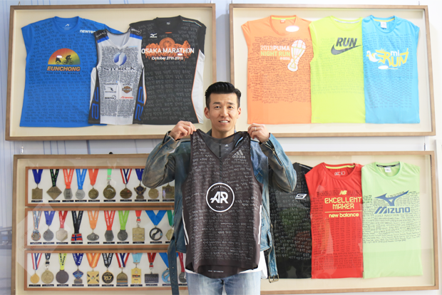 70여 개 대회의 증표 앞에서 365명의 이름이 적힌 티셔츠를 들고 웃고 있는 션 홍보대사.