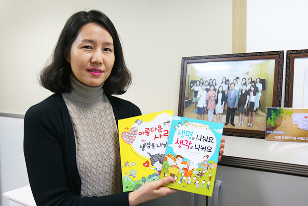 ▲ 어린이와 청소년의 눈높이에 맞춰 생명나눔을 쉽게 이해할 수 있도록 구성한 기획도서를 들고 있는 서윤경 국장. 뒤편의 사진은 나눔을 주제로 열린 독후감대회 시상식 모습.