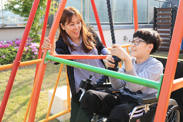엄마 옆에서 휠체어 그네를 타고 있는 장태환 어린이.